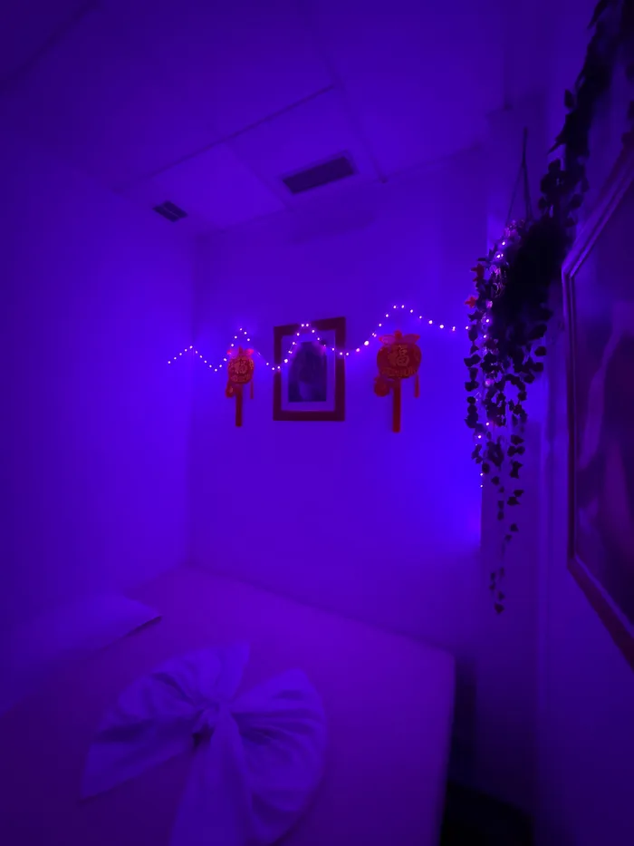 Sala de masaje con luz morada y una toalla doblada sobre la camilla